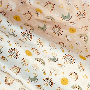 Pode incluir: Tecido branco com um padrão repetido de arco-íris, luas, estrelas, nuvens e sóis em tons de marrom, amarelo, verde e laranja.