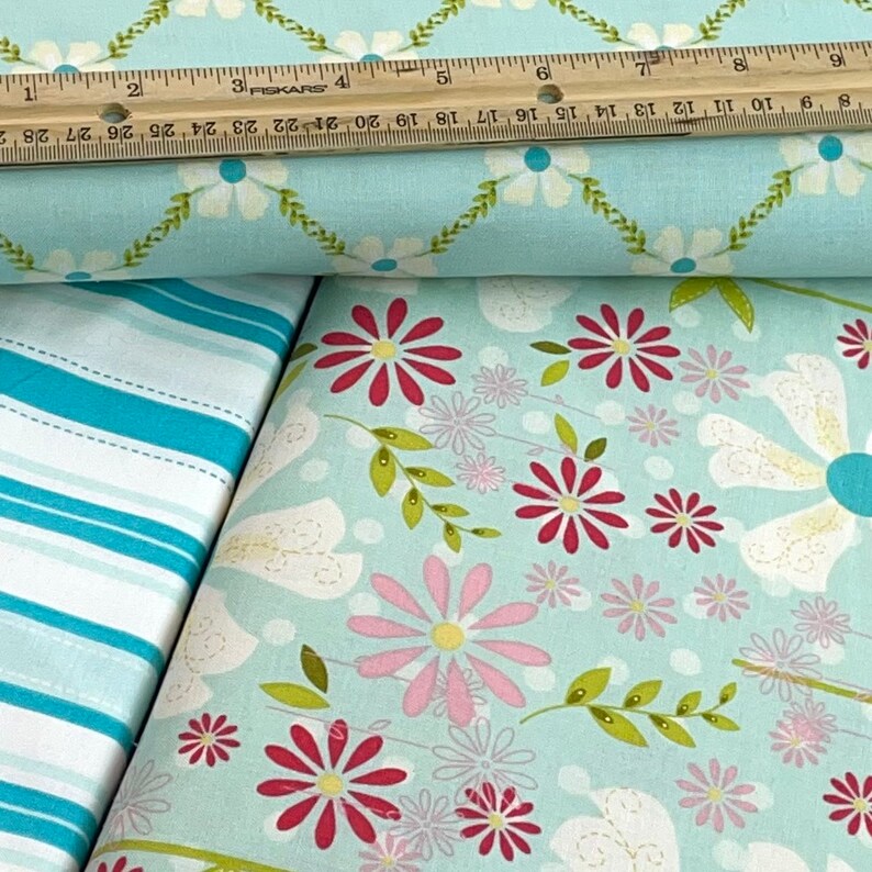 May include: Two pieces of fabric, one with a white and blue striped pattern and the other with a light blue background and a floral pattern with pink, red, and yellow flowers.
