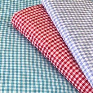 May include: Two pieces of checkered fabric, one red and white, and one blue and white, folded on top of a larger piece of blue and white checkered fabric.