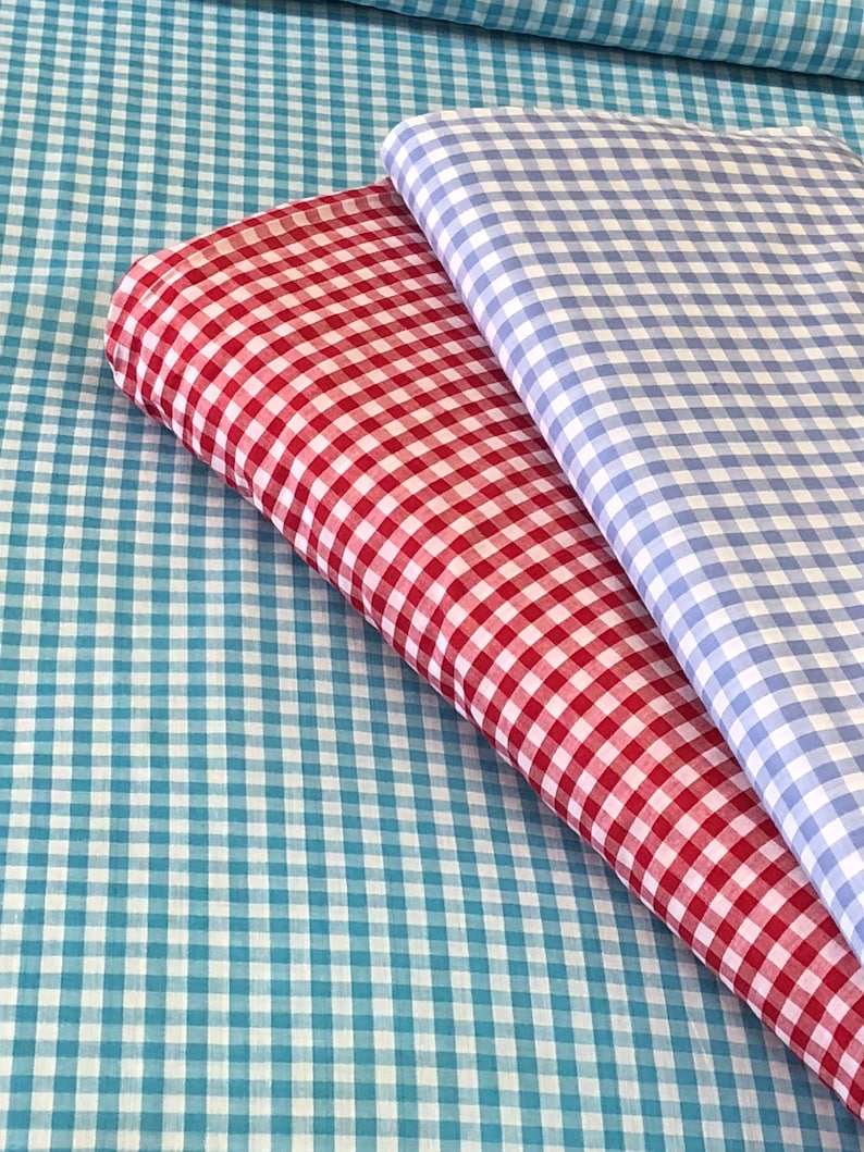 May include: Two pieces of checkered fabric, one red and white, and one blue and white, folded on top of a larger piece of blue and white checkered fabric.