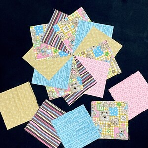 May include: A collection of 12 fabric squares with various patterns, including teddy bears, stars, stripes, and polka dots. The squares are in shades of blue, pink, brown, and yellow.