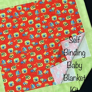 Op de afbeelding: Een groene en witte babydekenset van stof met een rode stof met een patroon van bouwvoertuigen. De set bevat zelfbindende randen en de tekst "Self Binding Baby Blanket Kit".