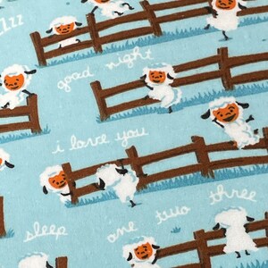 May include: A blue fabric with a repeating pattern of white sheep jumping over a brown fence. The text "good night", "i love you", "sleep", "one", "two", "three", and "zzz" is written on the fabric.