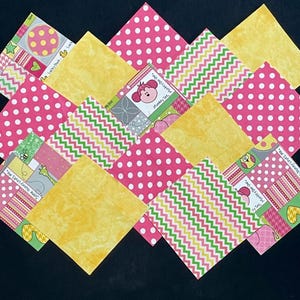 May include: A colorful patchwork quilt design featuring various patterned squares. Pink polka dots, yellow, and green zigzags are interspersed with squares displaying cartoon characters and text. The overall arrangement creates a visually appealing, geometric pattern.