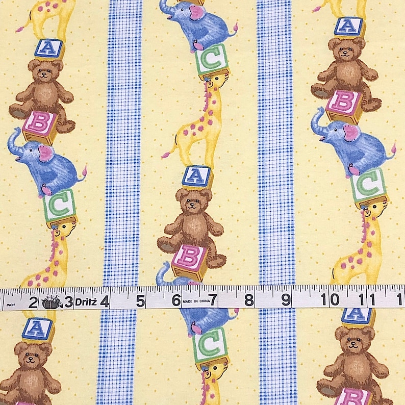 May include: Yellow fabric with a repeating pattern of blue and white stripes, yellow polka dots, and a stack of colorful blocks with a giraffe, elephant, and teddy bear on top. The blocks are labeled with the letters A, B, and C.