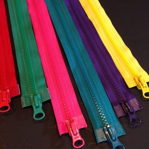May include: Assortment of colorful zippers in red, pink, green, teal, purple, and yellow. The zippers are laid out in a row on a black surface.