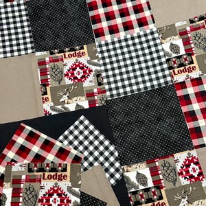 Può includere: Una trapunta patchwork con una varietà di motivi e colori. Il design include quadretti bianchi e neri, plaid rosso e nero, nero con pois bianchi e un tessuto beige con motivi di cervi e lodge. La parola "Lodge" è stampata su alcuni tessuti.
