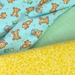 May include: Fabric samples featuring a light blue pattern with brown teddy bears, yellow stars, and green turtles. A second fabric is a solid green with white dots, and the third is yellow with white stars. The fabrics are likely for children's projects.