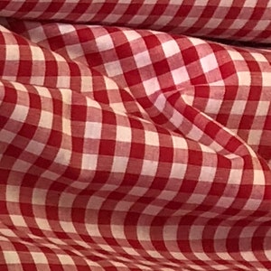 May include: Red and white gingham fabric with a checkered pattern. The fabric is folded and has a soft, textured look.