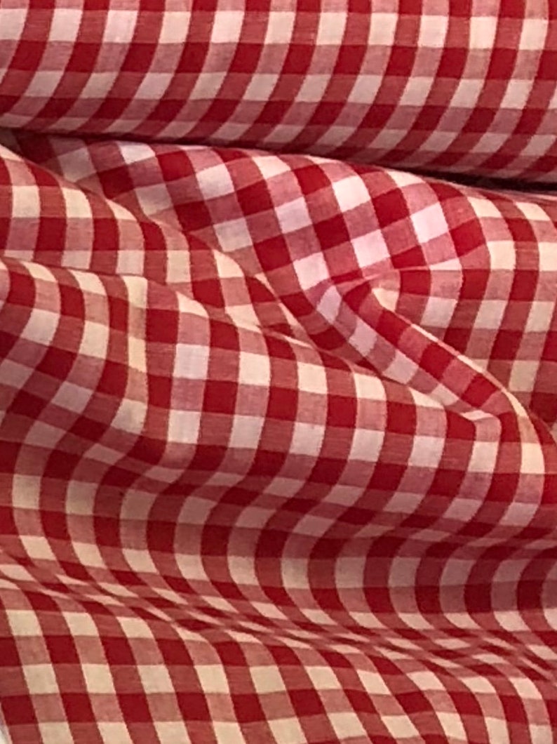 May include: Red and white gingham fabric with a checkered pattern. The fabric is folded and has a soft, textured look.