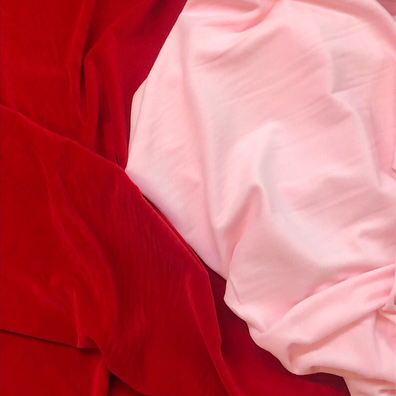 May include: Close-up of two fabric swatches, one red and one pink. The red fabric is a velvet with a soft, plush texture. The pink fabric is smooth and silky.