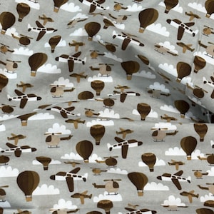 May include: Gray fabric with a repeating pattern of brown hot air balloons, airplanes, helicopters, and white clouds. The fabric is suitable for various sewing and crafting projects.