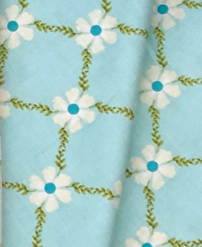 May include: A light blue fabric with a white floral pattern. The flowers have a blue center and are surrounded by green leaves.