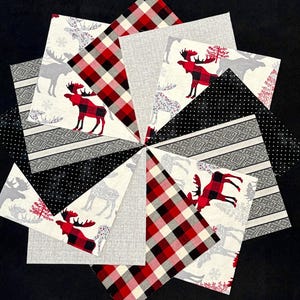 May include: A starburst design made from assorted fabric patterns. The fabrics display moose, snowflakes, and plaid in red, black, and grey. Some fabrics have a dotted or striped pattern. The background is black.