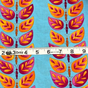 May include: A blue fabric with a repeating pattern of pink and orange butterflies with leaves. The fabric is measured with a ruler that reads "Dritz" and has markings in inches.