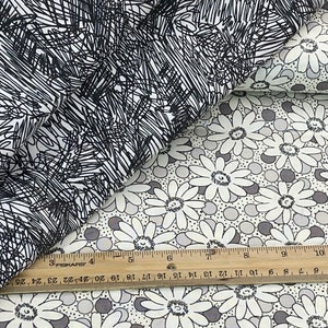May include: Two fabric swatches, one with a black and white scribble pattern and the other with a white daisy pattern on a light gray background with gray dots.