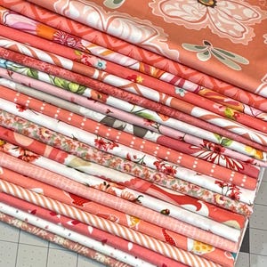 May include: A stack of folded fabric with various floral and patterned designs in shades of coral, pink, and white. The fabrics feature large flowers, stripes, and polka dots, suitable for quilting or sewing projects.