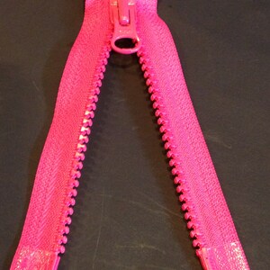 May include: A bright pink zipper with a metal slider. The zipper is open and the teeth are visible.