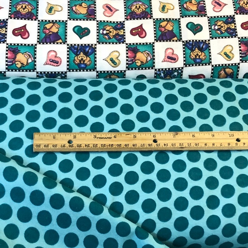 May include: Teal fabric with a white background and a pattern of large teal polka dots. A ruler is placed on the fabric, showing the scale in inches.