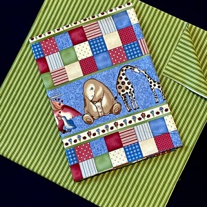 Op de afbeelding: Een blauwe en groene patchwork stof met een rand van rood, wit en blauw. De stof heeft verschillende dieren, waaronder een beer, een giraffe en een vogel. De stof is perfect voor quilten, naaien of knutselen.