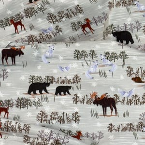 May include: A light gray fabric featuring a winter forest scene. The design includes black bears, brown moose, red deer, white foxes, and owls. The trees are brown, and snowflakes are scattered across the background.