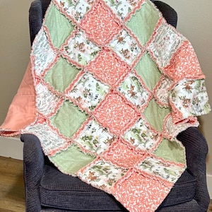 May include: A handmade patchwork quilt with a diamond pattern. The quilt features squares of light green, white with floral and animal prints, and coral with leaf patterns. The quilt is draped over a dark blue armchair.