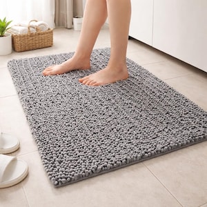 May include: A grey rectangular bath mat with a textured, plush surface. The mat is approximately 60 cm long and 40 cm wide. The image shows a person standing on the mat.