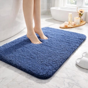 Puede incluir: Una alfombra de baño rectangular azul marino con una superficie gruesa y texturizada. La imagen muestra a una persona de pie sobre la alfombra en un baño. Se ven zapatillas blancas en el fondo.