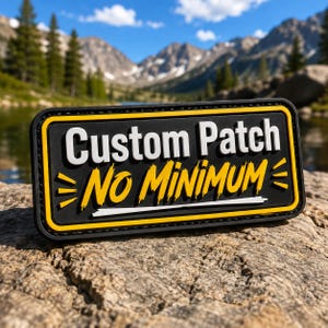 Peut inclure: Un écusson rectangulaire noir avec une bordure jaune, affichant le texte blanc Custom Patch et le texte jaune NO MINIMUM. Le design comprend des accents graphiques jaunes sur les côtés et une ligne horizontale blanche sous le texte jaune.