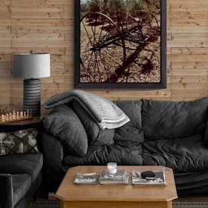 Puede incluir: Un salón con un sofá gris oscuro, una mesa de centro de madera y un cuadro enmarcado de una rueda de carro antigua. Una lámpara gris y un juego de ajedrez están sobre una mesa auxiliar. La pared es de tablones de madera.