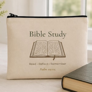 May include: A cream-colored canvas zipper pouch featuring the text Bible Study, an illustration of an open book, the words Read - Reflect - Remember, and the scripture reference Psalm 119:105 printed in a dark brown color on the front surface.