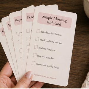 Pode incluir: Um conjunto de cartões retangulares em tom off-white com cantos arredondados, apresentando um cabeçalho rosa suave intitulado Simple Morning with God. O cartão lista cinco caixas de seleção com tarefas como respirar, agradecer e orar.