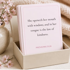 May include: A stack of light pink rectangular cards with a thin border, featuring the black printed text: She openeth her mouth with wisdom; and in her tongue is the law of kindness. PROVERBS 31:26. The cards are housed in a small, open beige box.