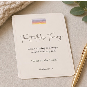 May include: A rectangular off-white card featuring a small watercolor sunset graphic at the top. The text reads: Trust His Timing, God's timing is always worth waiting for, Wait on the Lord, and Psalm 27:14. A gold metallic pen lies beside the card.