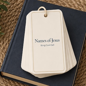May include: A stack of off-white rectangular cards held together by a beige ring. The top card features a thin gold border and the dark blue text "Names of Jesus" followed by "Ring Card Set" in a smaller font size below the main title.