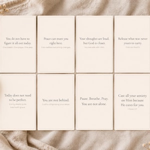 May include: Eight cream-colored affirmation cards with black text on a beige linen surface. Each card features a different inspirational quote. The cards are arranged in two rows of four. Dried flowers and a ceramic vase are in the background.