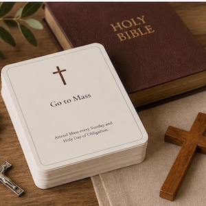 May include: A deck of white rectangular cards with rounded corners, featuring a brown cross icon, the text "Go to Mass," and the instruction "Attend Mass every Sunday and Holy Day of Obligation." The cards are displayed alongside a brown Holy Bible, a wooden cross, and a rosary with light-colored beads and a silver-toned crucifix.