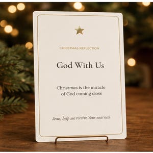 May include: A rectangular white card with a gold border and a gold star at the top. The text reads: CHRISTMAS REFLECTION, God With Us, Christmas is the miracle of God coming close, and Jesus, help me receive Your nearness. The card sits on a gold stand.