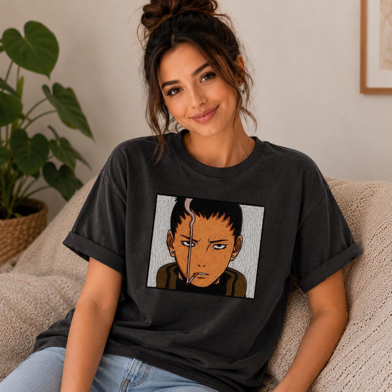 Pu&ograve; includere: T-shirt grigio scuro con una grafica quadrata di un personaggio anime con una sigaretta. Il personaggio ha i capelli scuri, una cicatrice e un'espressione seria. La maglietta ha maniche corte e una vestibilit&agrave; rilassata.
