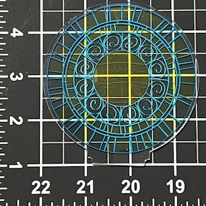 May include: A clear, circular craft with a blue and teal clock face design. The design features lines, swirls, and the text "Soothing Bird Studios". The craft is on a black and white grid.