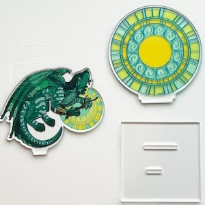 May include: Acrylic dragon and stained glass-style circle art pieces. The dragon is green with a yellow clock. The circle art has a yellow centre and teal and yellow accents. A clear acrylic stand is also included.