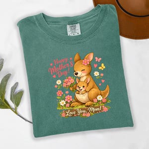 May include: Green Comfort Colors t-shirt featuring a cartoon kangaroo and joey with flowers. Text reads "Happy Mother's Day! Love You, Mom!" The design includes pink hearts and butterflies. The shirt is a size L-G-G.