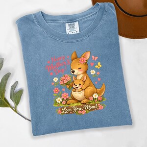 May include: A light blue t-shirt featuring a cartoon kangaroo with a joey in its pouch, surrounded by flowers and butterflies. The text "Happy Mother's Day!" and "Love You, Mom!" are displayed in pink.