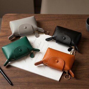 May include: Four small, rectangular, pebbled-texture pouches in grey, black, green, and orange. Each pouch features a front flap with a snap button closure, a top zip, and a gold-toned metal key ring attached to the side with a short chain.