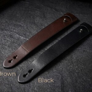 May include: Two leather wristbands, one brown and one black, each featuring a smooth surface, a single metallic stud closure, and two keyhole-shaped adjustment holes at the tapered end. The text Brown and Black is printed below each item.
