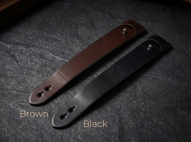 May include: Two leather wristbands, one brown and one black, each featuring a smooth surface, a single metallic stud closure, and two keyhole-shaped adjustment holes at the tapered end. The text Brown and Black is printed below each item.