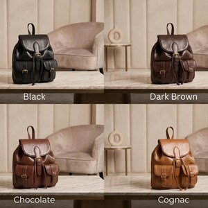 May include: A collection of leather backpacks in four colors: black, dark brown, chocolate, and cognac. Each backpack features a flap closure, two front pockets, and adjustable straps. The text below each backpack indicates its color.