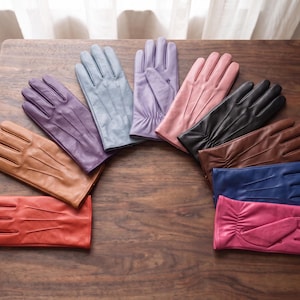 May include: A collection of ten leather gloves arranged in a semi-circle, featuring a variety of colours including red, tan, purple, light blue, lavender, pink, black, brown, dark blue, and magenta, each with three stitched lines on the back.