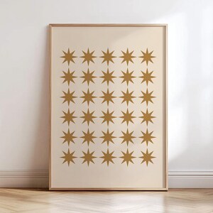 May include: A rectangular framed wall art print featuring a grid of thirty golden-brown eight-pointed stars arranged in six rows and five columns against a solid light beige background, enclosed within a thin, light-toned wooden frame.