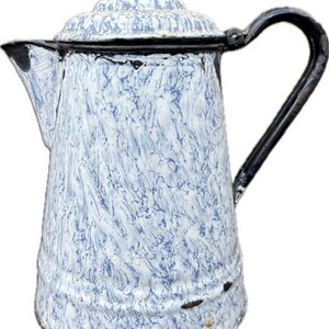 May include: A tall, cylindrical enamel coffee pot featuring a white and light blue marbled pattern. The vessel includes a matching lid with a small knob, a curved spout, and a sturdy black handle. The rim and base edges show signs of wear.